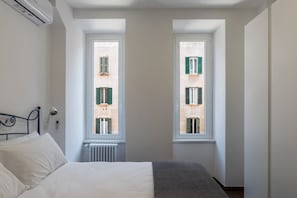 A bedroom with a bed, a radiator, and two windows with shutters.
