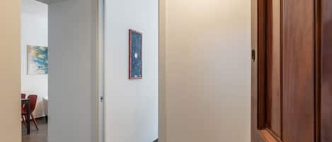 Un pasillo con una puerta de madera, una pequeña mesa con sillas y un cuadro en la pared.