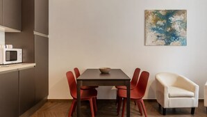 A modern dining area with a dark wooden table, red chairs, a white armchair, and a microwave on a shelf. - Testaccio 11 - FromHometoRome (Roma)