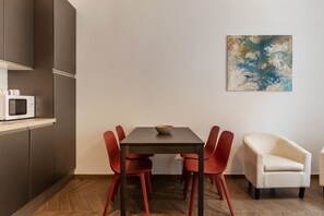 A modern dining area with a dark wooden table, red chairs, a white armchair, and a microwave on a shelf. - Testaccio 11 - FromHometoRome (Roma)