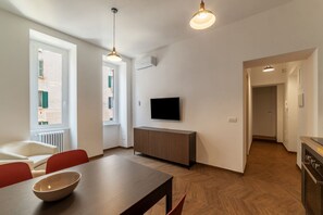 Un saló modern amb zona de menjador, un televisor fixat a la paret i una cuina visible a través d'una obertura.