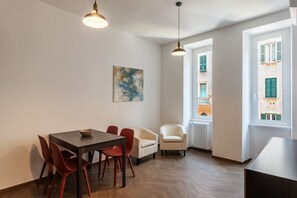 A dining area with a table, chairs, pendant lights, a radiator, and a window with a view of buildings.