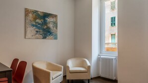 A room with a wooden floor, a beige armchair, a red chair, and a window with a view of a building. - Testaccio 11 - FromHometoRome (Roma)