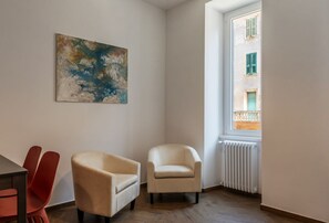 A room with a wooden floor, a beige armchair, a red chair, and a window with a view of a building. - Testaccio 11 - FromHometoRome (Roma)