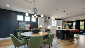 A modern kitchen with a central island, green upholstered chairs, and pendant lighting.