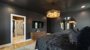 A modern bedroom with a large bed, a wooden dresser, a flat-screen TV, and a chandelier.