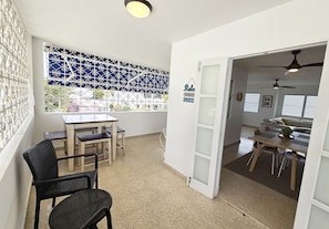 A room with a dining table, chairs, a window with decorative metal bars, and a door leading to another room.