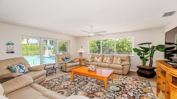 Amplia sala de estar con un sofá color beige, una mesa de centro y un ventanal con vista a una piscina.