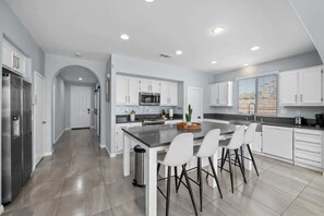 A modern kitchen with white cabinets, a central island with bar stools, and a stainless steel refrigerator.