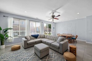 Ein modernes Wohnzimmer mit Ecksofa, Hocker und Essbereich mit Tisch und Stühlen.