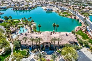 A large house with a swimming pool, surrounded by palm trees and a lake.