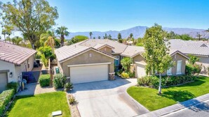 A residential neighborhood with houses featuring red-tiled roofs, well-maintained lawns, and a clear view of mountains in the background. - Private Pool & Hot Tub | Indian Palms 3BR (Indio)