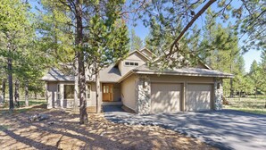 A two-story house with a stone facade, a garage, and a well-maintained lawn. - 37 Kinglet - North End River Charmer! Hot Tub, SHARC, Ping Pong, Bikes (Sunriver)