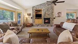 A cozy living room with a stone fireplace, leather sofas, a wooden coffee table, and a television. - 37 Kinglet - North End River Charmer! Hot Tub, SHARC, Ping Pong, Bikes (Sunriver)