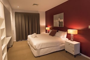 Ein Hotelzimmer mit einem Bett, zwei Nachttischen mit Lampen, einem Kleiderschrank und einem großen Fenster mit Vorhängen.