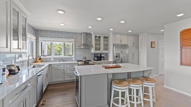 Una cocina moderna con armarios grises, una isla grande con taburetes y un ventanal que proporciona luz natural.