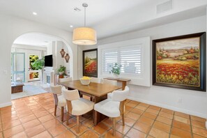 A dining area with a wooden table and white chairs, a large painting on the wall, and a view of a garden through the window. - The Canal Escape - canal-front Italian villa (Los Angeles)
