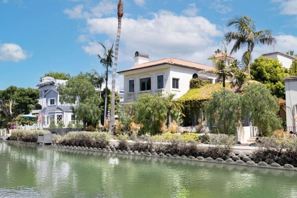 A waterfront property with a white building, palm trees, and a small dock. - The Canal Escape - canal-front Italian villa (Los Angeles)