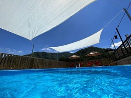 A swimming pool with a wooden deck and a white canopy.