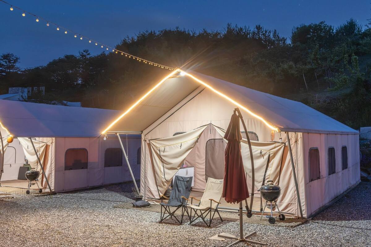 A tented camping area with a grill and chairs.
