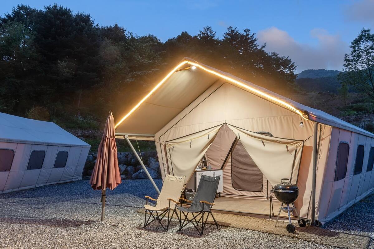 A tent with a lighted roof, a folding chair, and a grill outside.