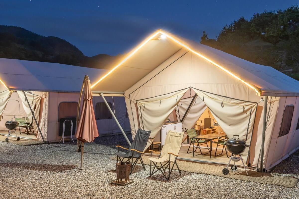 A large, well-lit tent with a dining area inside, surrounded by gravel.