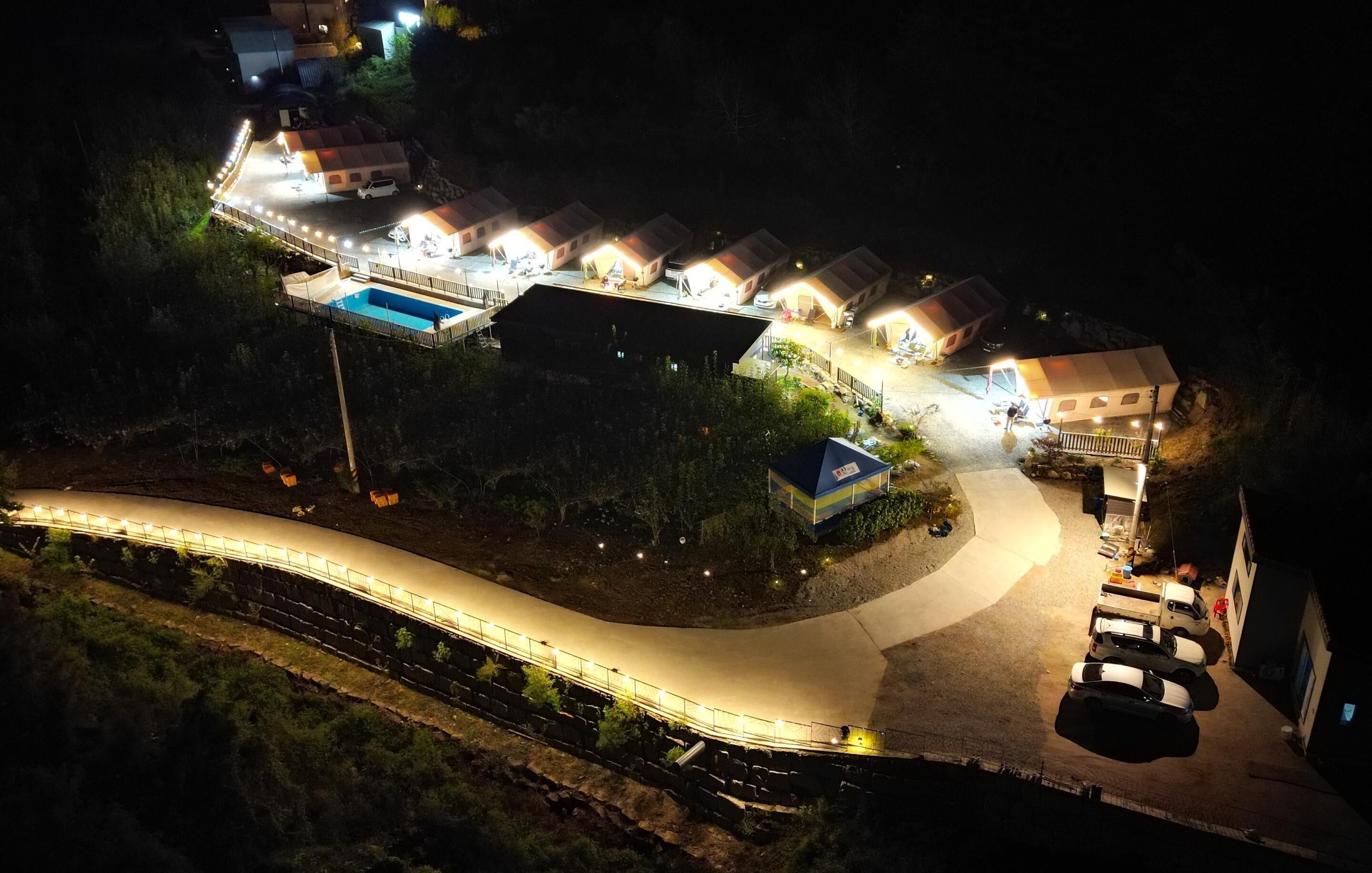 A well-lit resort with multiple cottages, a swimming pool, and a winding road.
