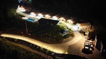 A well-lit resort with multiple cottages, a swimming pool, and a winding road.