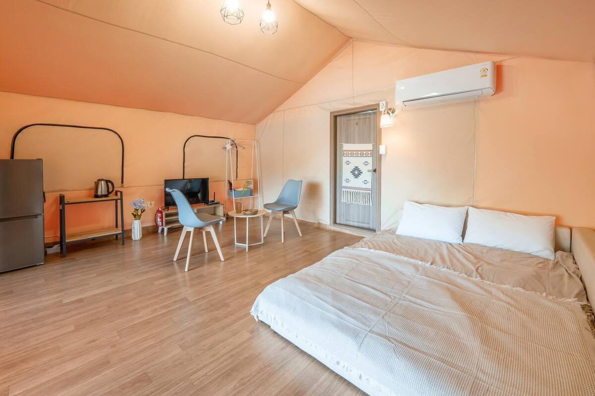 A bedroom with a bed, a desk with a TV, a chair, and an air conditioning unit.