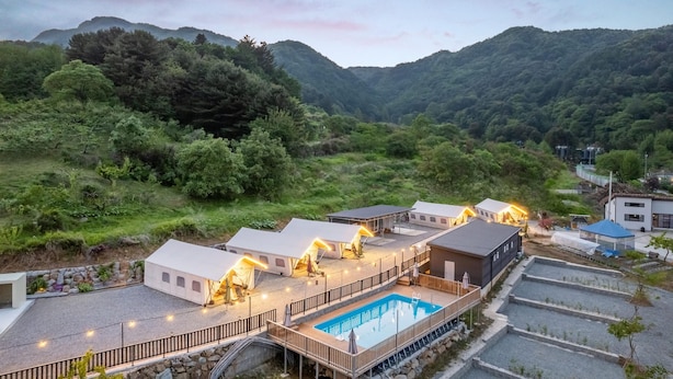 A resort with multiple cabins, a swimming pool, and a view of the surrounding forest and hills. - Gapyeong Sanmaeul Glamping (Gapyeong)