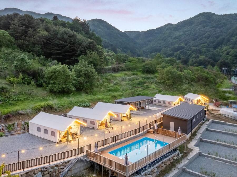 Ein Resort mit mehreren Hütten, einem Schwimmbad und Blick auf den umliegenden Wald und die Hügel.