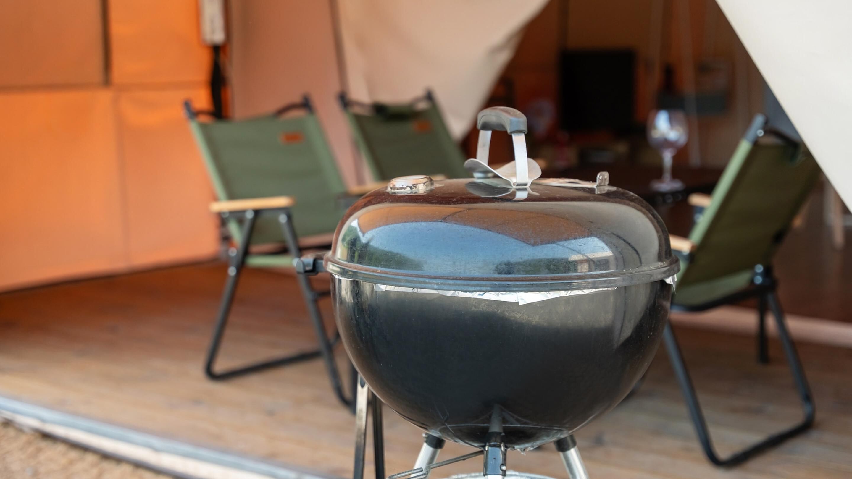 A portable grill with a lid, set on a metal stand, in an outdoor dining area with chairs and a table.