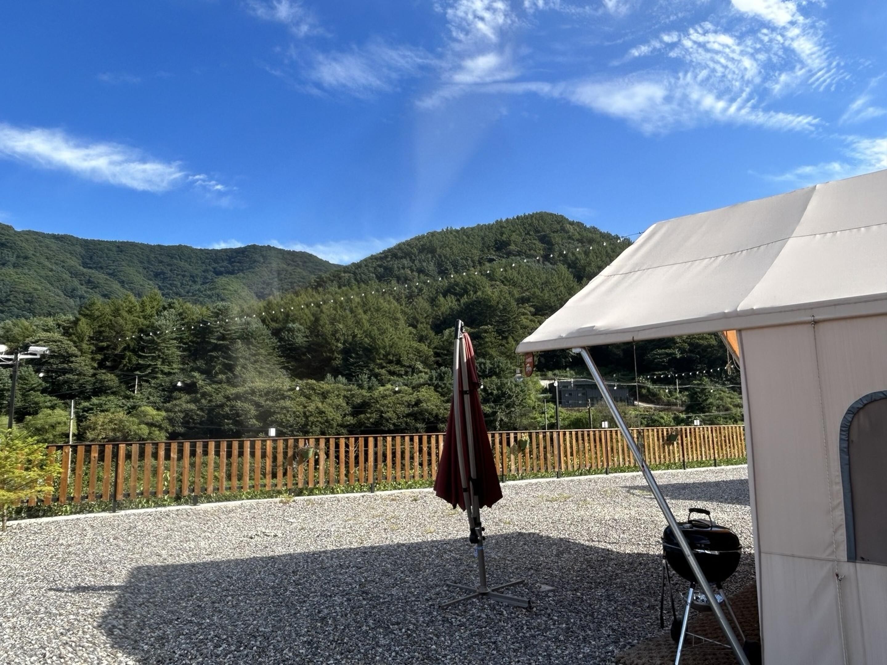 A patio area with a barbecue grill, a tent, and a wooden fence overlooking a forested mountain.