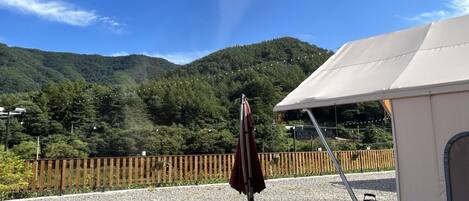 A patio area with a barbecue grill, a tent, and a wooden fence overlooking a forested mountain.