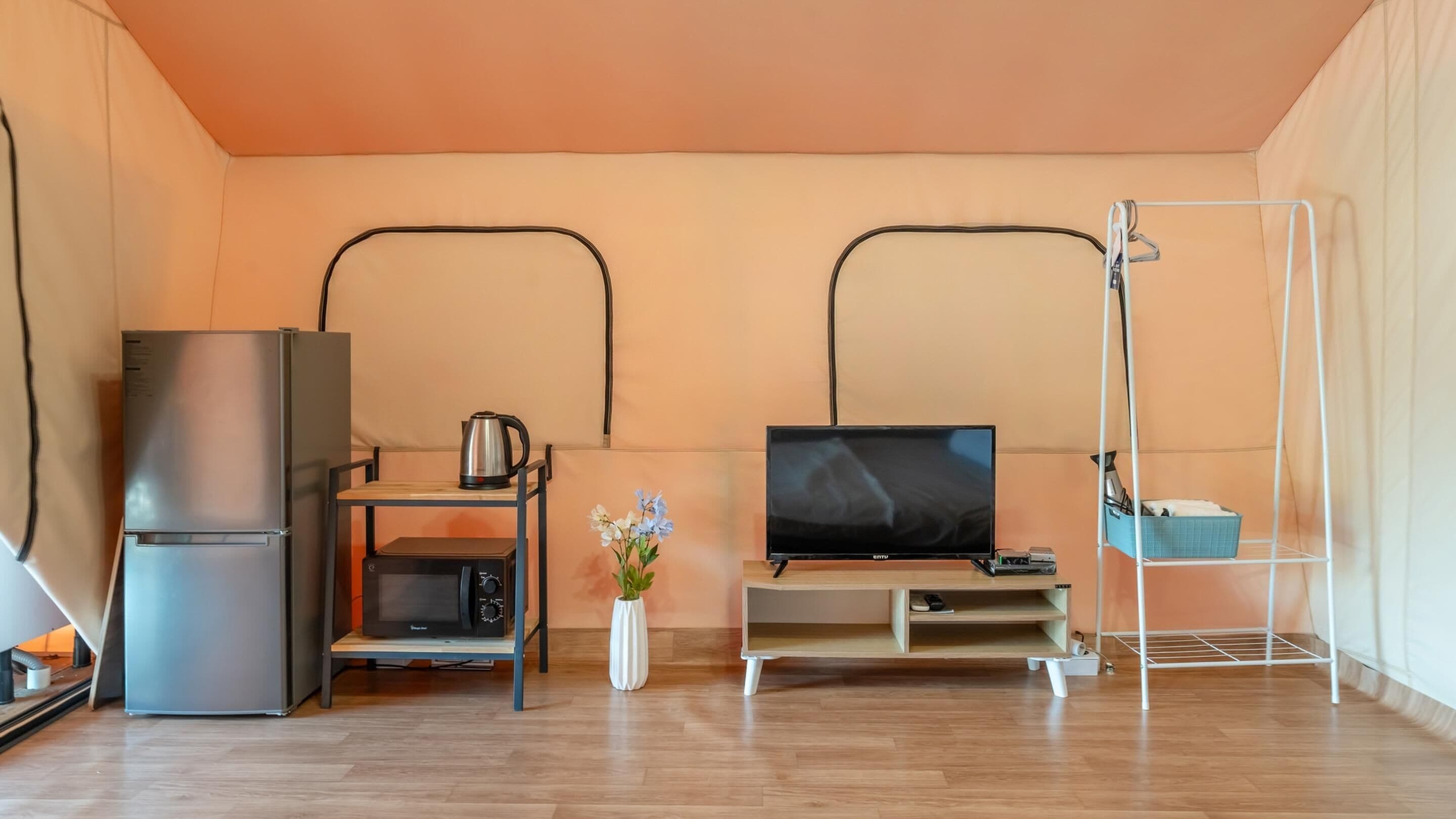 Un espacio habitable compacto con kitchenette, televisor de pantalla plana, una mesita y un estante blanco.