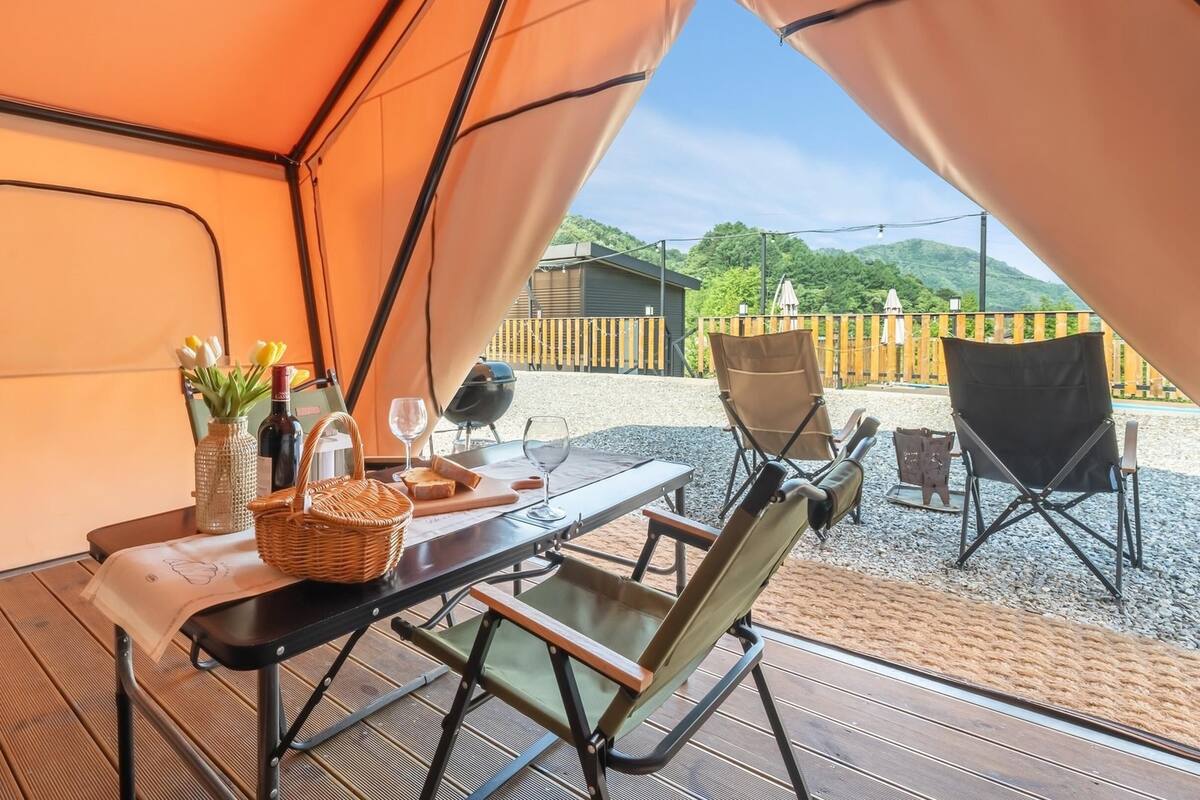 A tented outdoor area with a table set for two, including a bottle, glasses, and a basket.