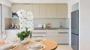 A modern kitchen with white cabinets, a stainless steel refrigerator, and a dining table set with plates and glasses. - Luxury 1-Br. apartment, sea view, parking. (Vallauris)