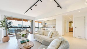 A modern living room with a sofa, armchair, and coffee table, a balcony with a view, and a kitchen in the background. - Luxury 1-Br. apartment, sea view, parking. (Vallauris)