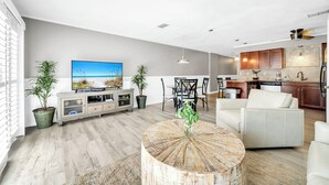 Een moderne woonkamer met een flatscreen televisie, een ronde salontafel en een eethoek met een tafel en stoelen.