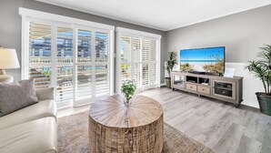 Een moderne woonkamer met een grote televisie, een ronde salontafel en uitzicht op het balkon.