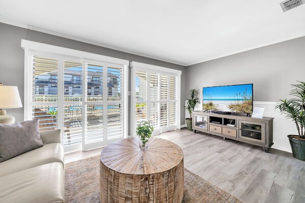 A modern living room with a large TV, a round coffee table, and a view of the balcony.