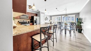 Een moderne keuken met granieten aanrechtbladen, roestvrijstalen apparatuur en een eethoek met een houten tafel en barstoelen.