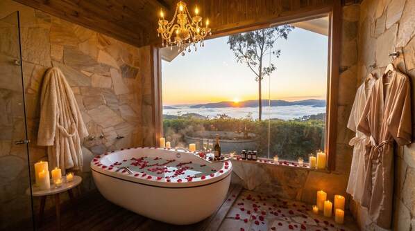 Un baño con una bañera grande, paredes de piedra, vistas al atardecer y un candelabro.