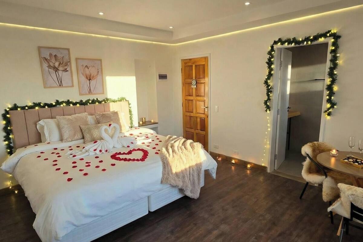 A hotel room with a bed, a small table with a bottle of champagne and glasses, and a chair.