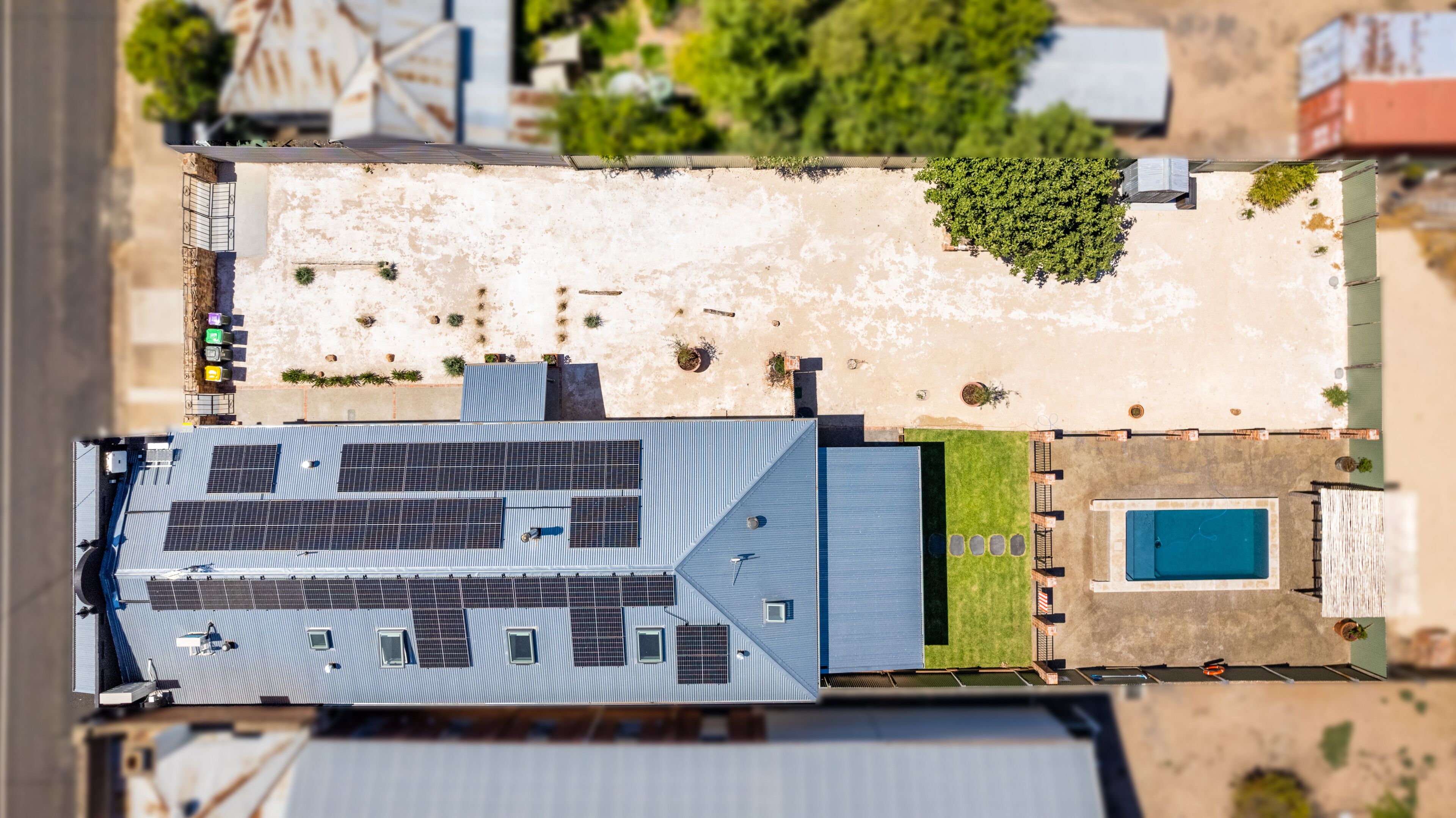 Vue aérienne d’un bâtiment doté d’un grand toit, de panneaux solaires, d’une piscine et d’un espace verdoyant environnant.