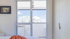 A bedroom with a bed, a window with a view of buildings, and a door. - Ycp2307 in S o Paulo (São Paulo)