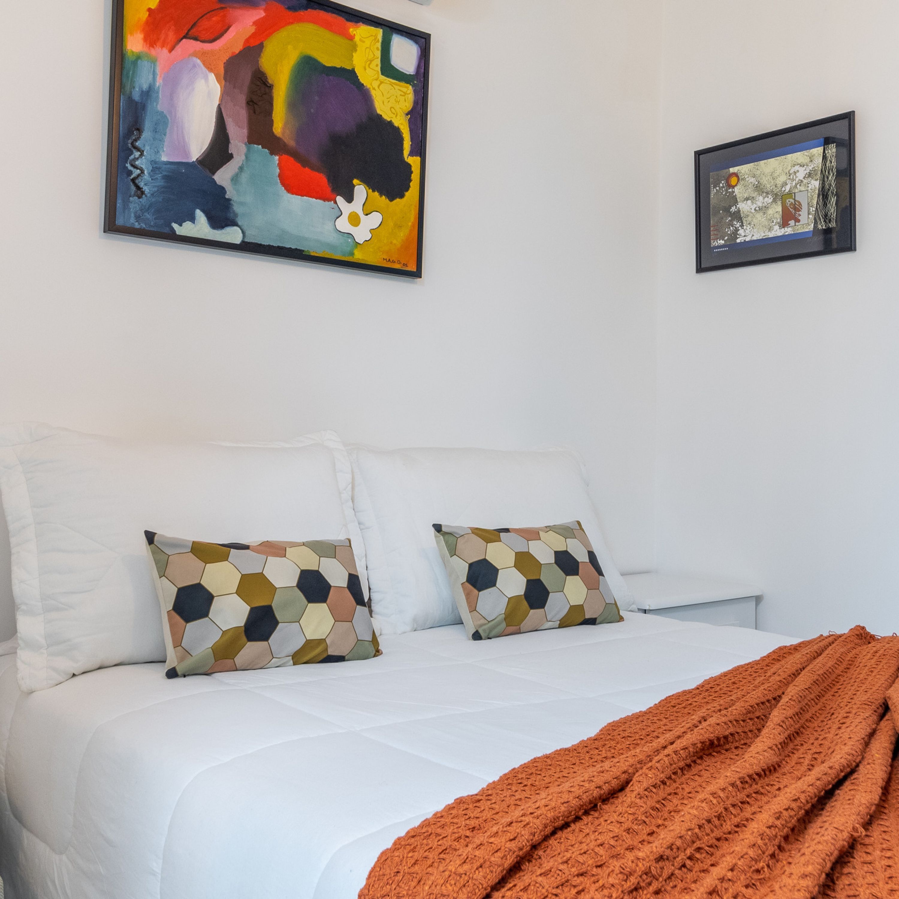 Un dormitorio con una cama, dos almohadas, un edredón y dos obras de arte en la pared.