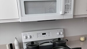 Una cocina con microondas, estufa y dos ollas sobre la hornilla.