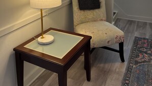 Una habitación con una mesa de madera, una lámpara, una silla con estampado floral y un espejo grande en la pared.
