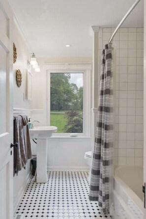 A bathroom with a window, a toilet, a sink, and a shower area.